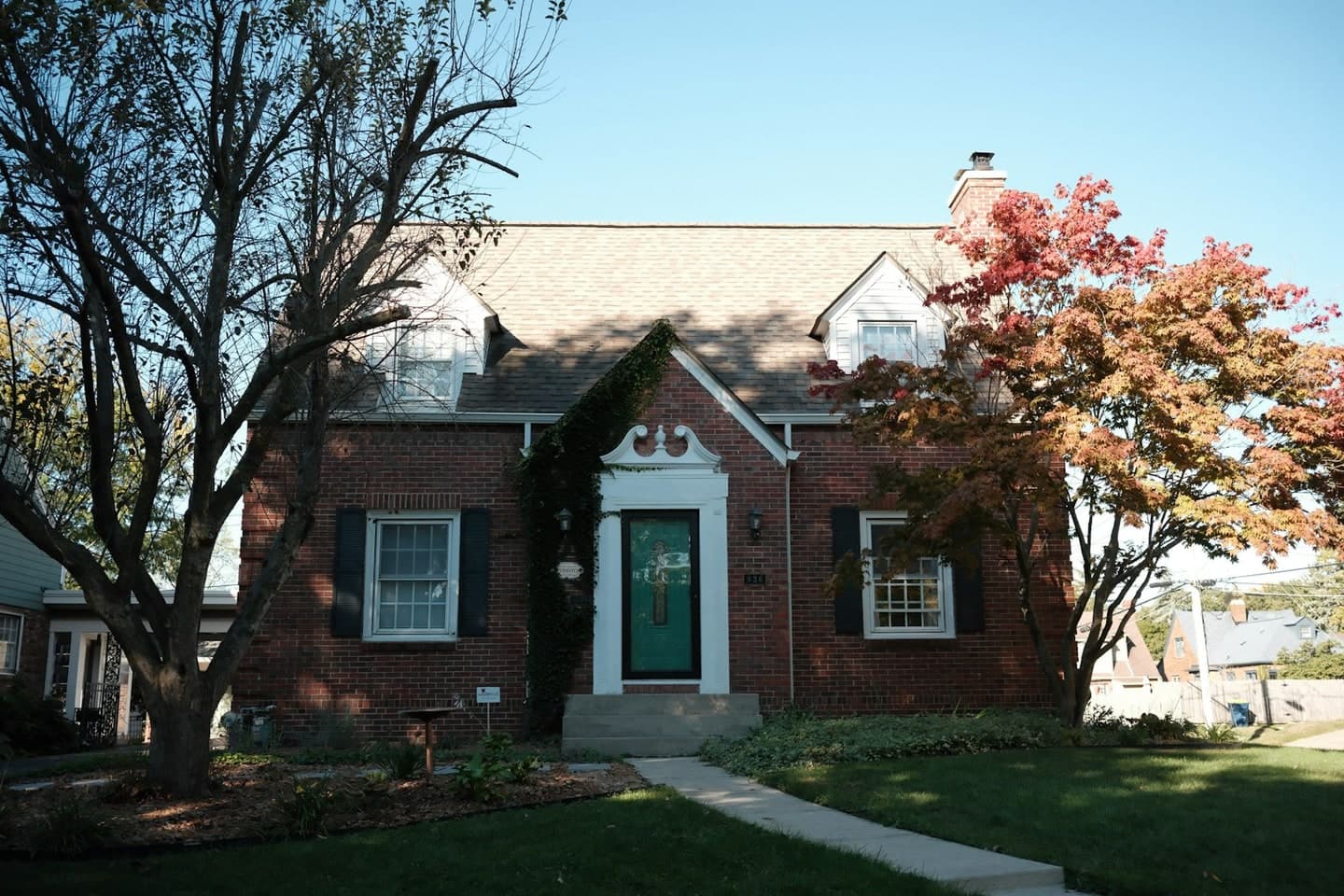 A brick house with a front walk and autumn trees on a quiet residential street