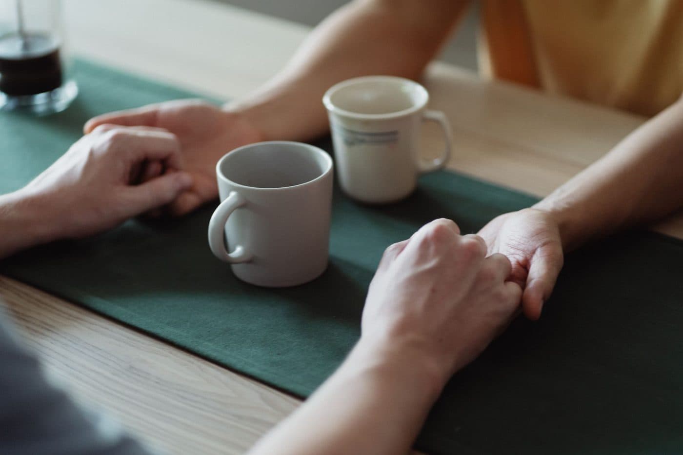 Two people holding hands across a table during a supportive conversation
