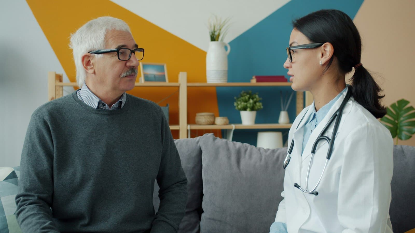 A clinician sits with an older man on a sofa and talks through his visit
