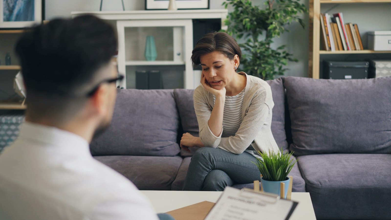 A counselor listens to a client on a sofa in a calm office