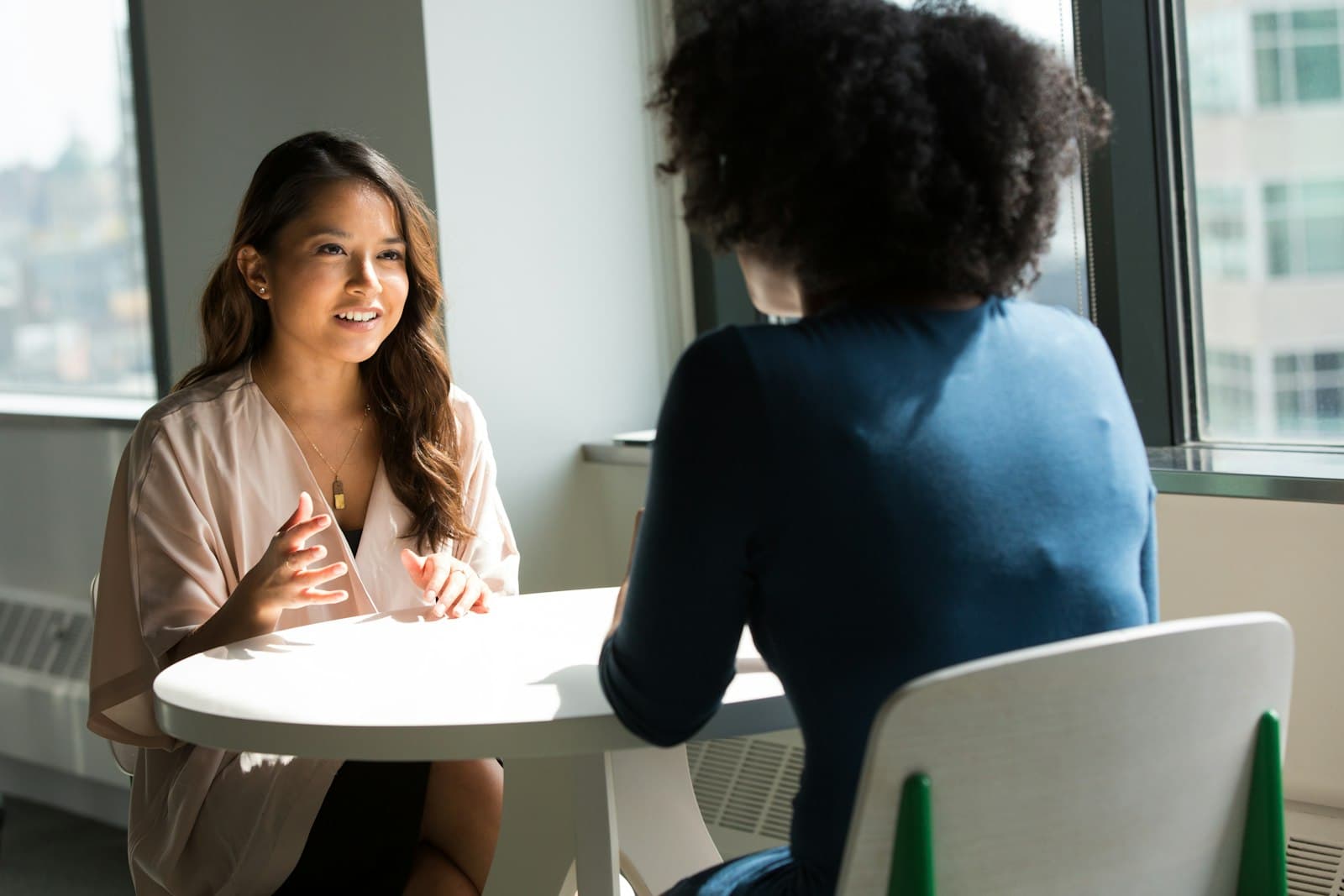 Two women talk across a small table in a bright office
