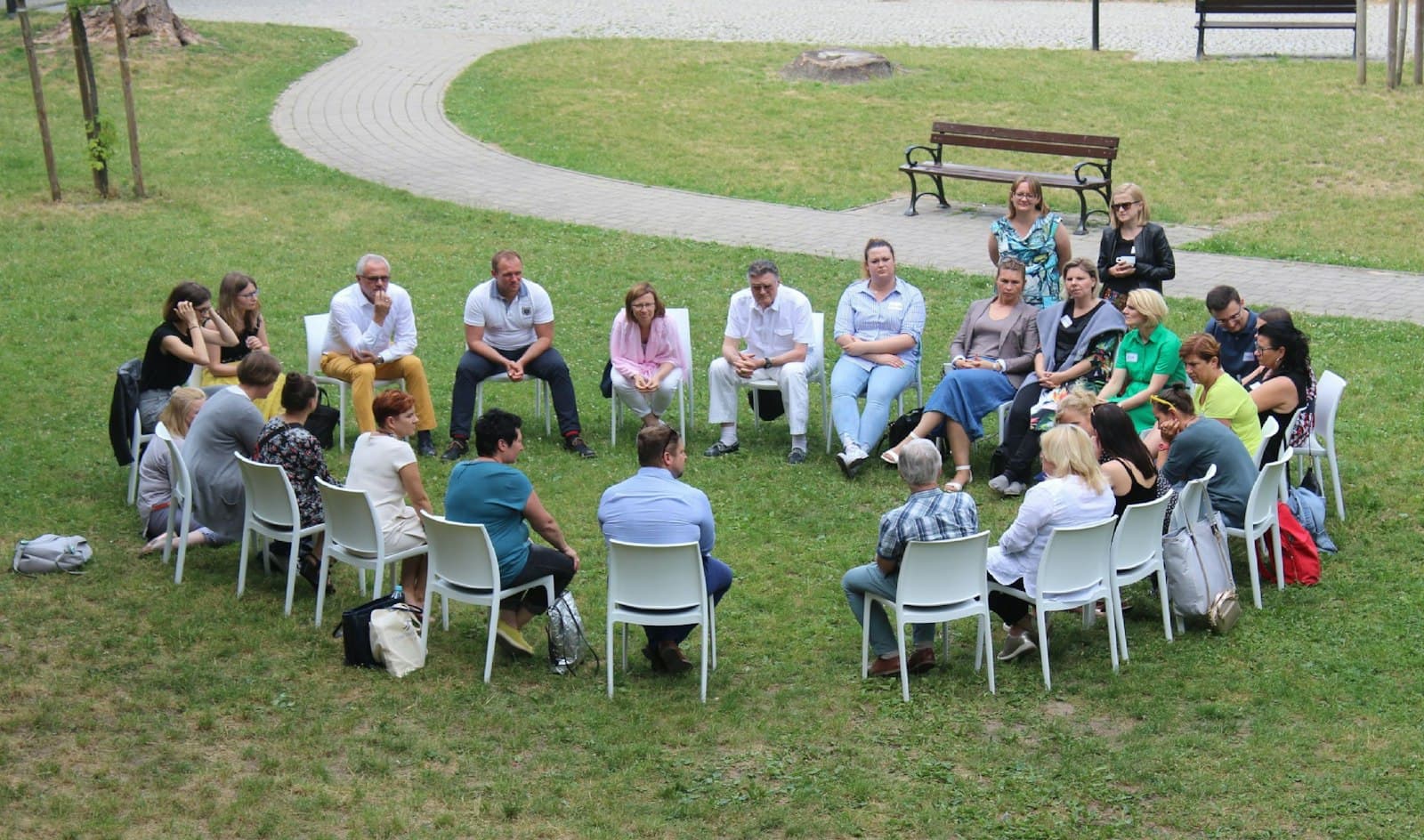 A community support group sitting in a circle of chairs on a lawn
